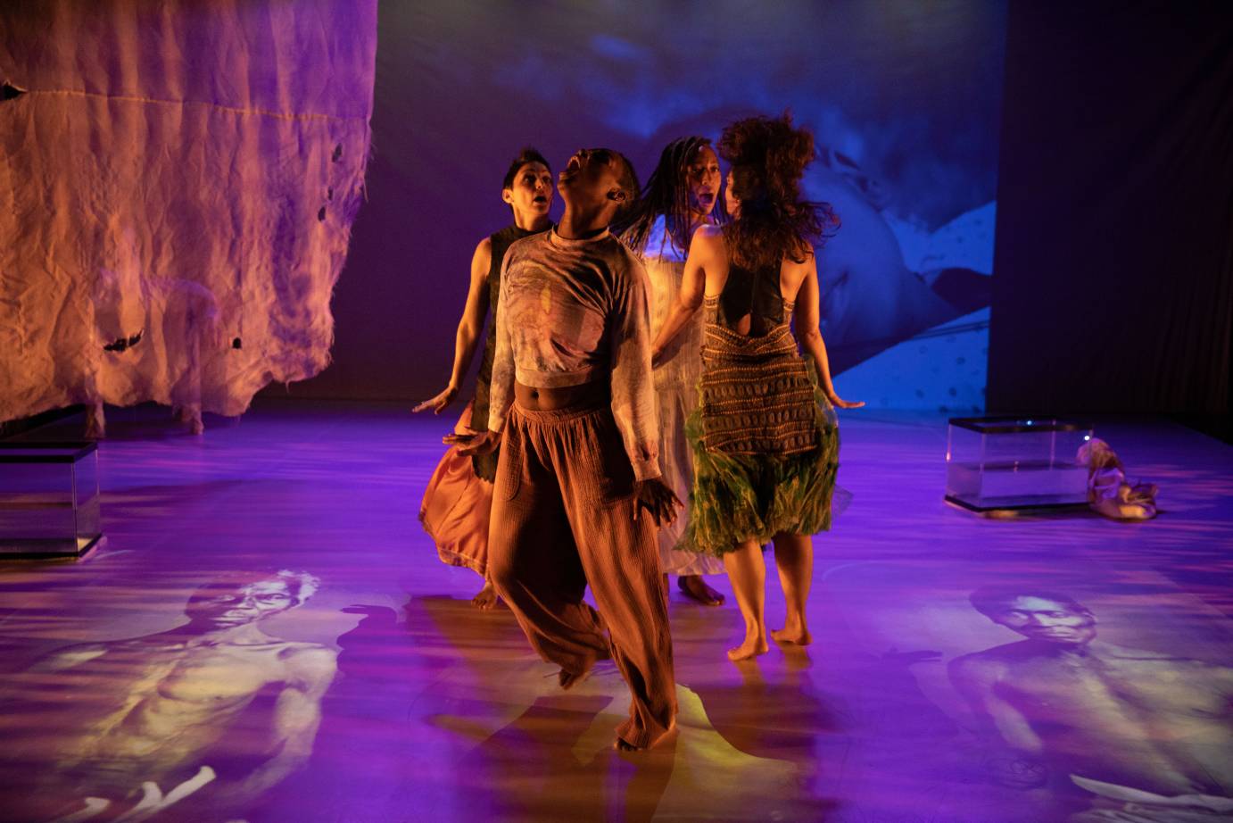 Four dancers stand in a small circle, their mouths open